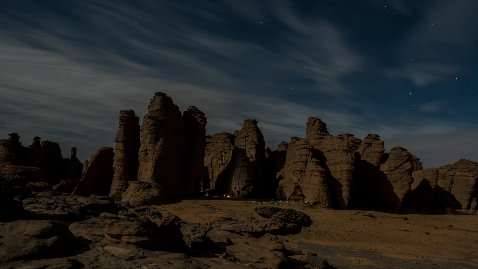 Torres de arenisca bajo un cielo oscuro con estrellas y nubes alargadas.
